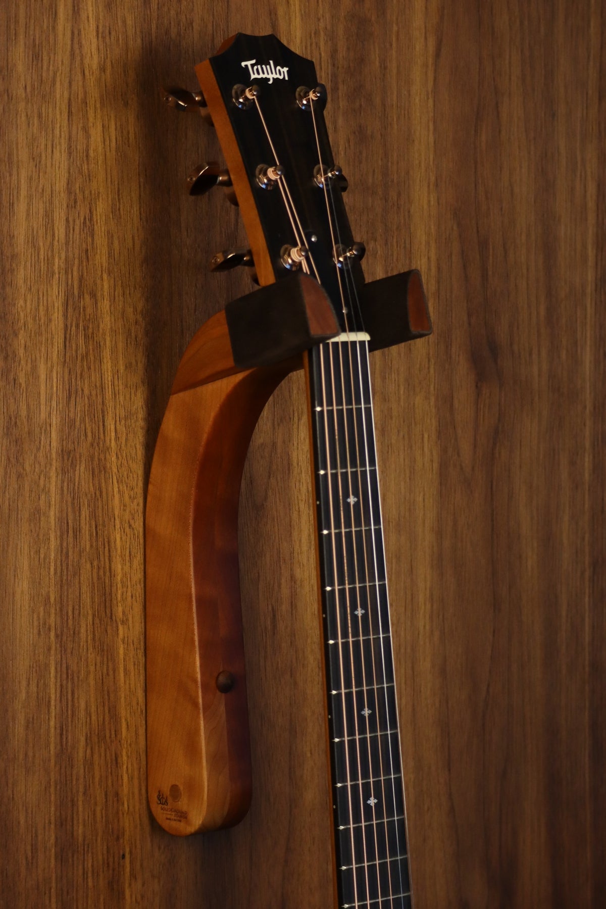 Cherry wood guitar wall mount hanger installed on paneled wall with Taylor guitar