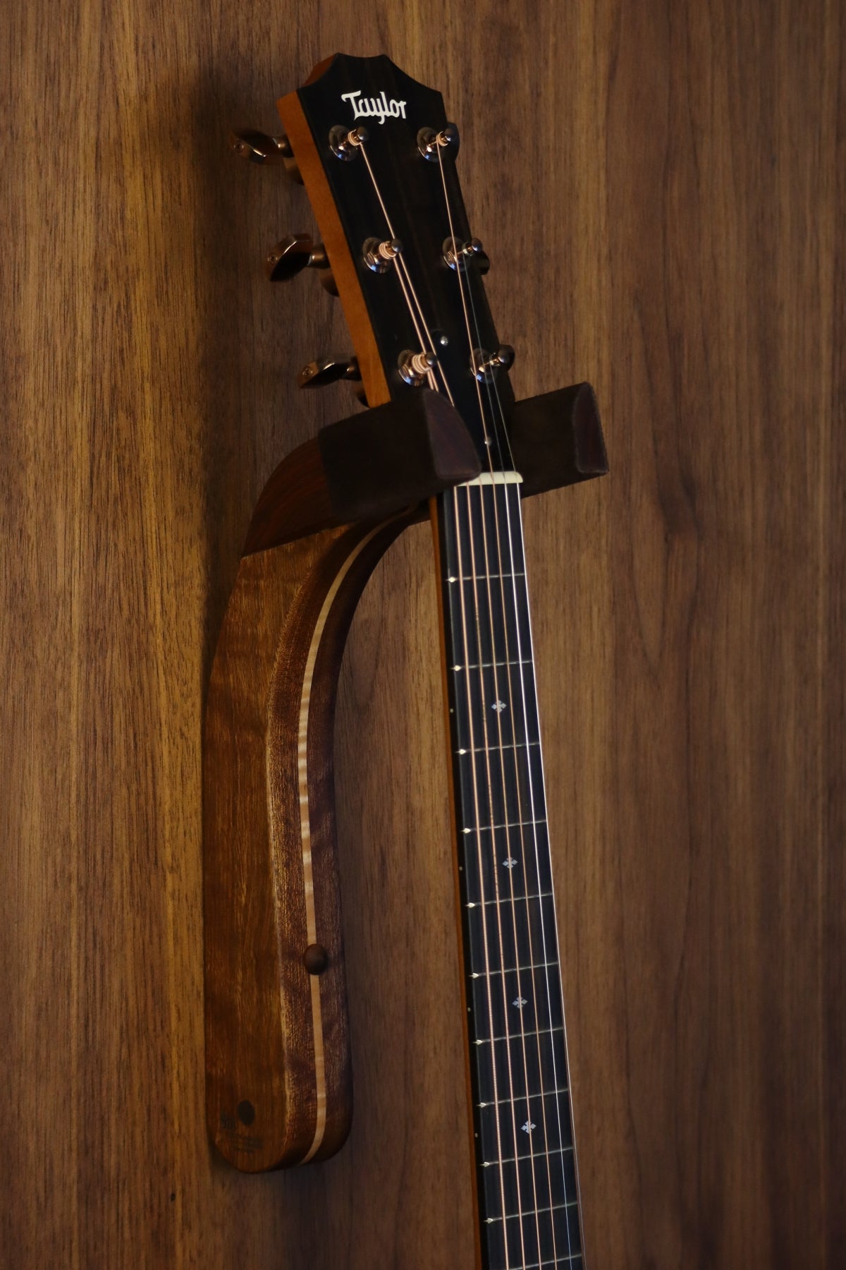 Chechen Caribbean rosewood and curly maple wood guitar wall mount hanger installed on paneled wall with Taylor guitar