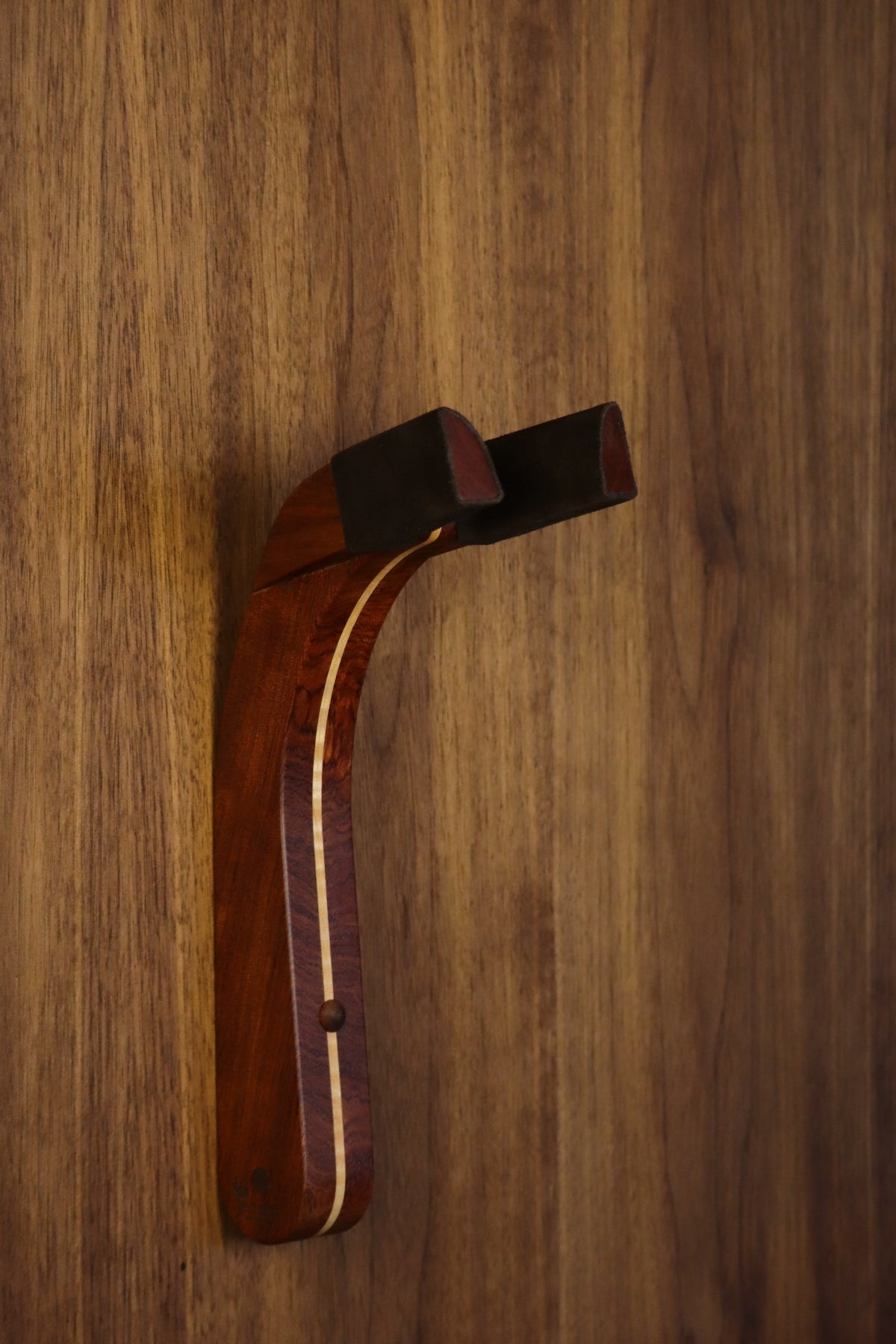Bubinga rosewood and curly maple wood guitar wall mount hanger installed on paneled wall