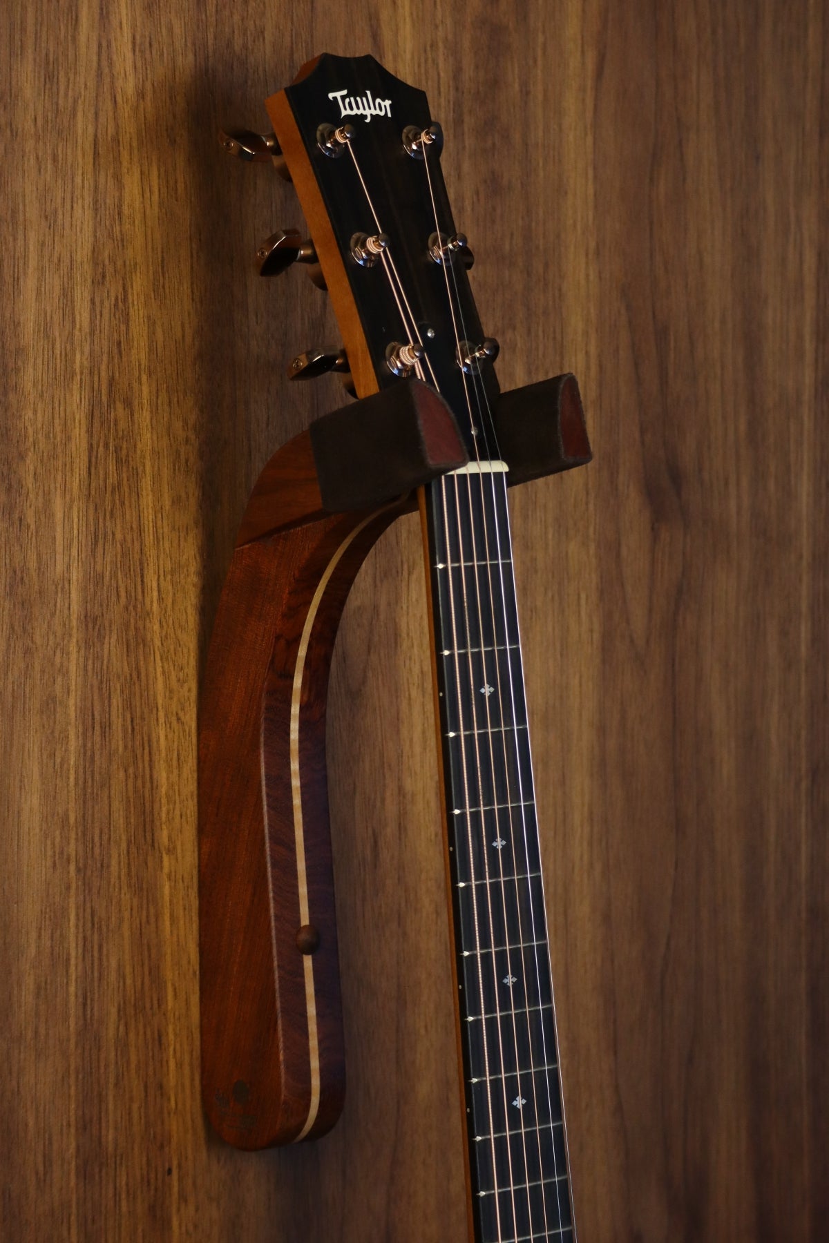Bubinga rosewood and curly maple wood guitar wall mount hanger installed on paneled wall with Taylor guitar