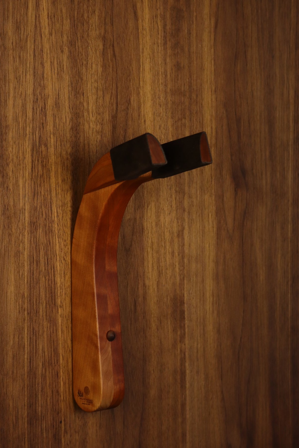 Cherry wood guitar wall mount hanger installed on paneled wall
