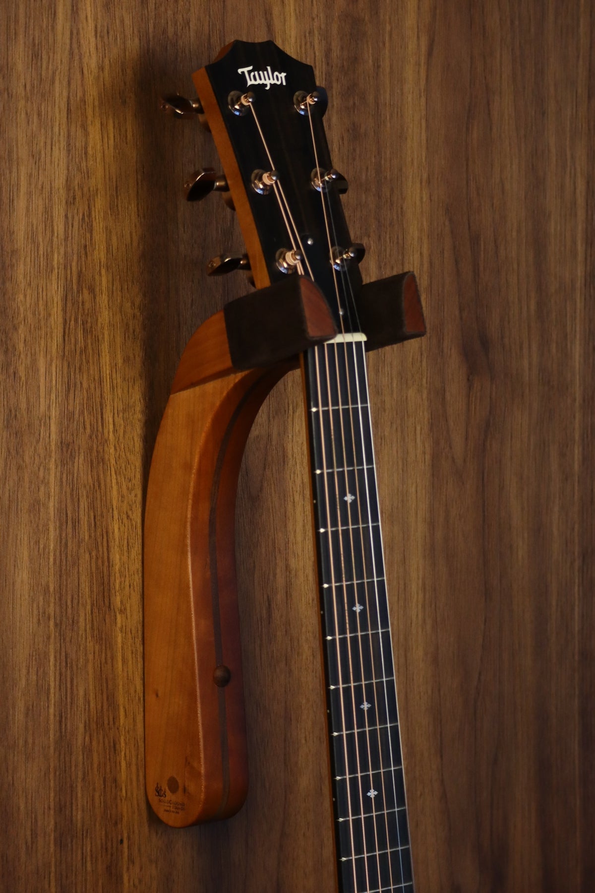 Cherry and walnut wood guitar wall mount hanger installed on paneled wall with Taylor guitar