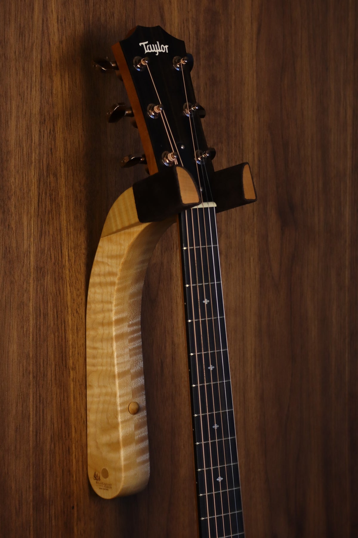 Curly maple wood guitar wall mount hanger installed on paneled wall with Taylor guitar