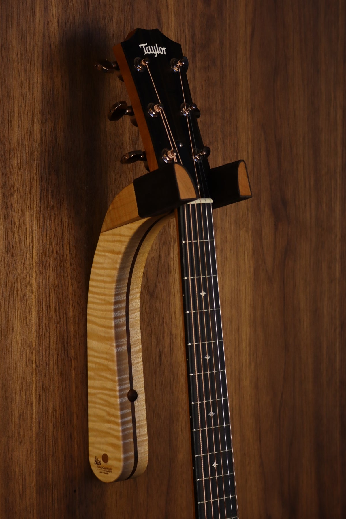 Curly maple and walnut wood guitar wall mount hanger installed on paneled wall with Taylor guitar