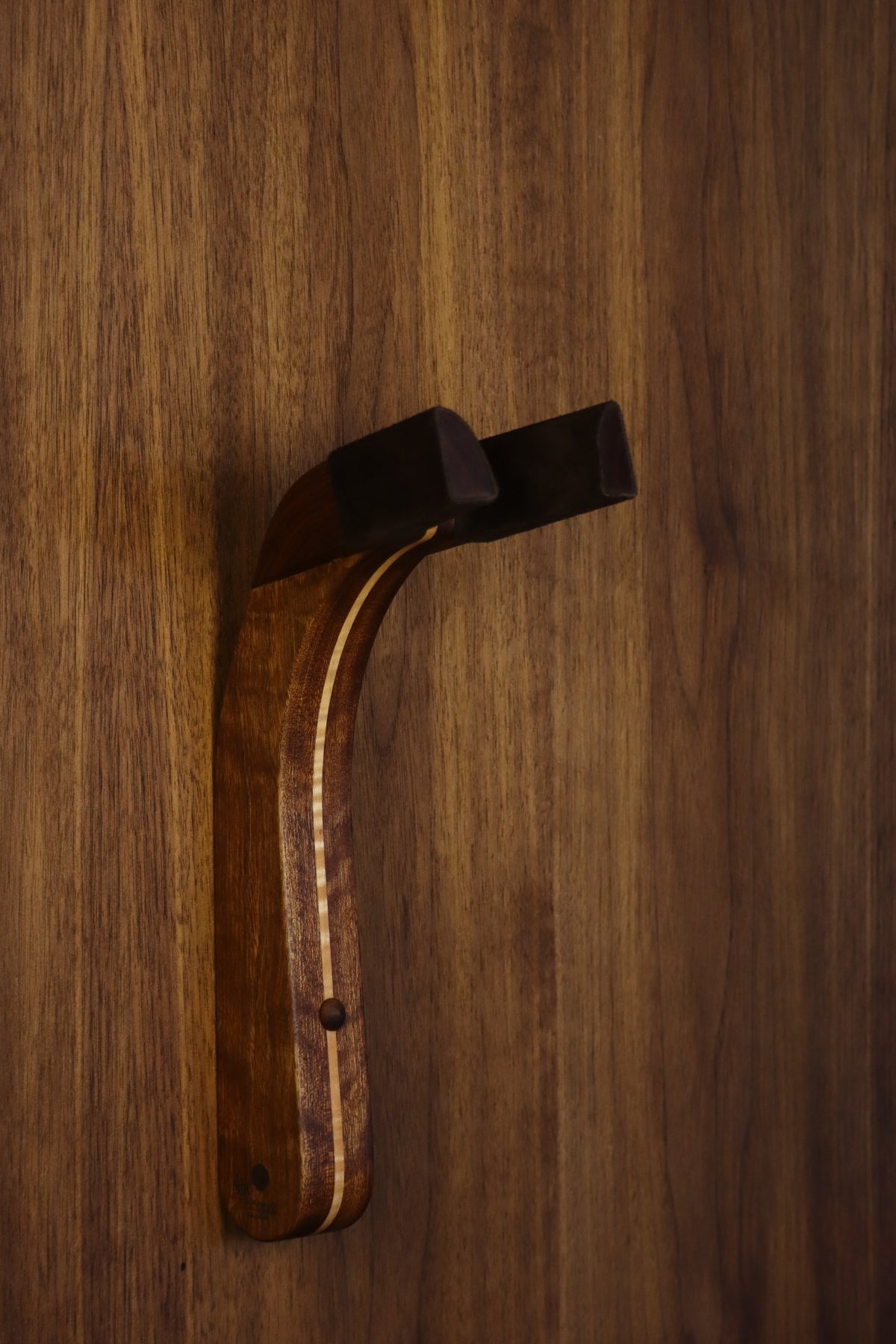 Chechen Caribbean rosewood and curly maple wood guitar wall mount hanger installed on paneled wall