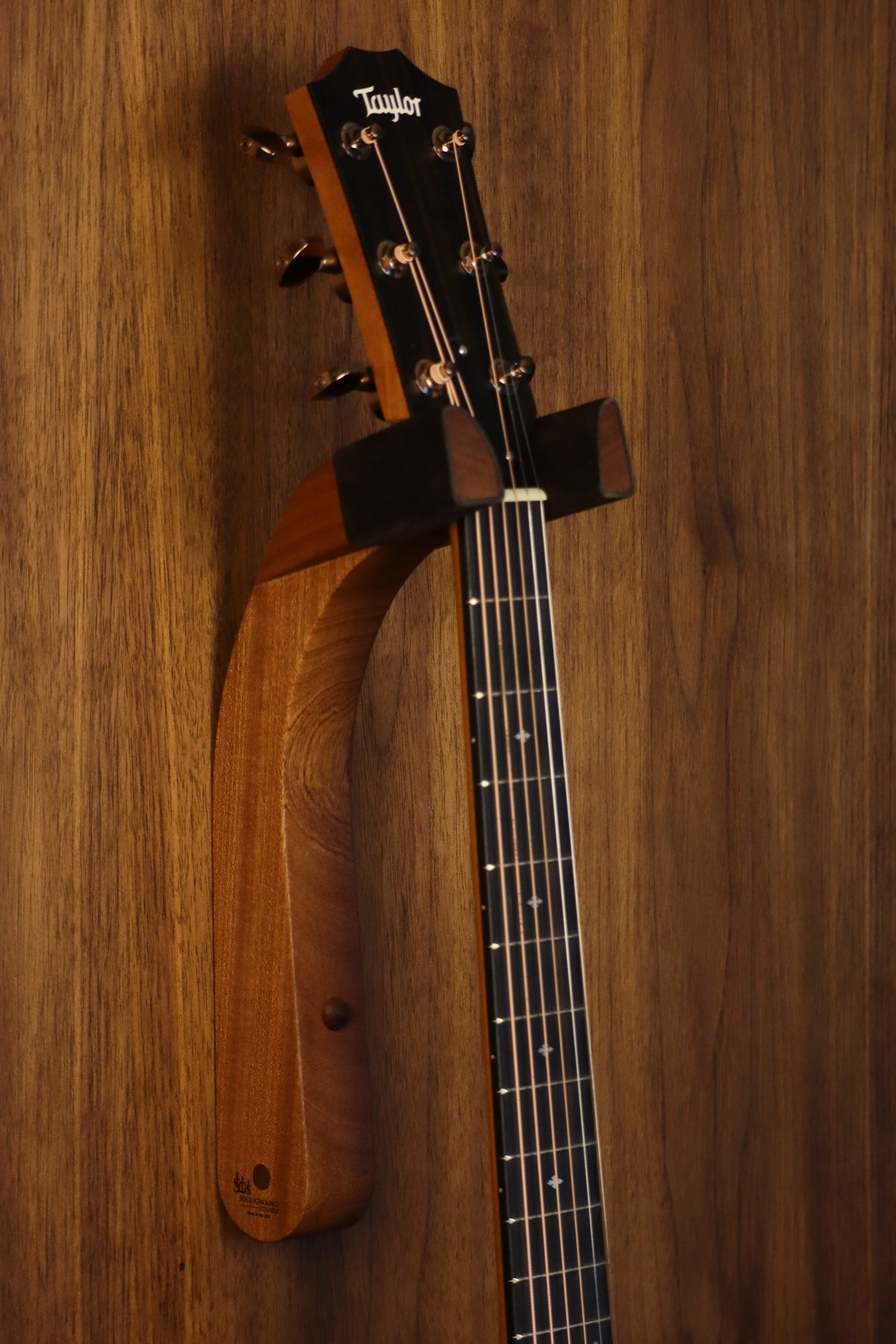 Sapele mahogany wood guitar wall mount hanger installed on paneled wall with Taylor guitar