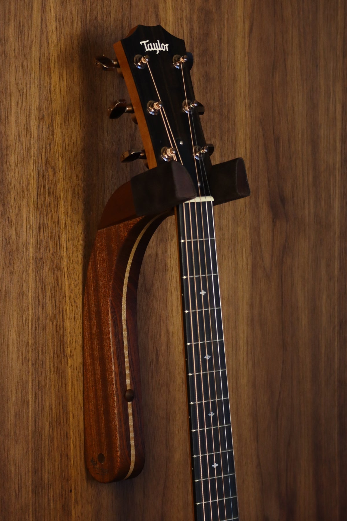 Sapele mahogany and curly maple wood guitar wall mount hanger installed on paneled wall with Taylor guitar