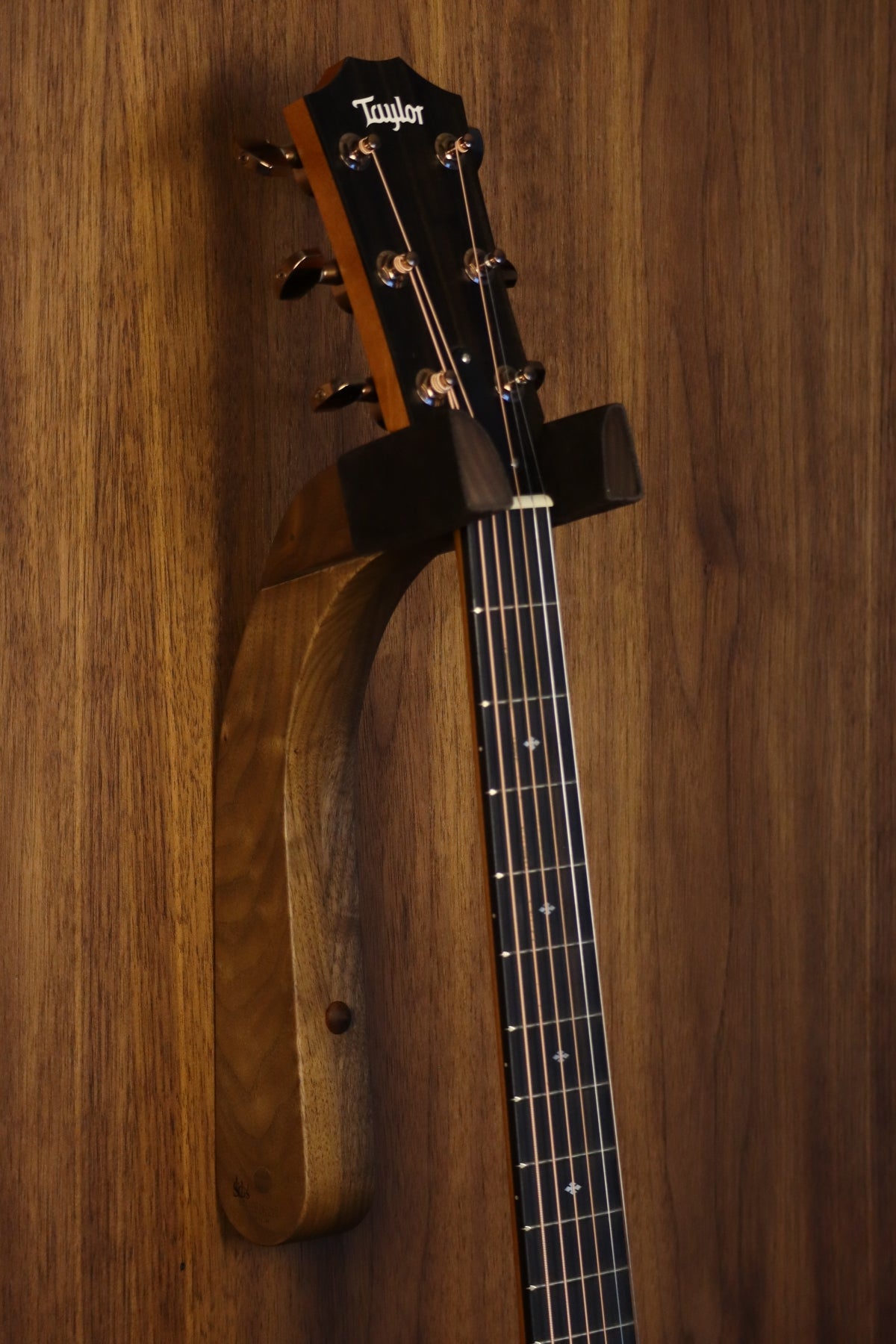 Walnut wood guitar wall mount hanger installed on paneled wall with Taylor guitar