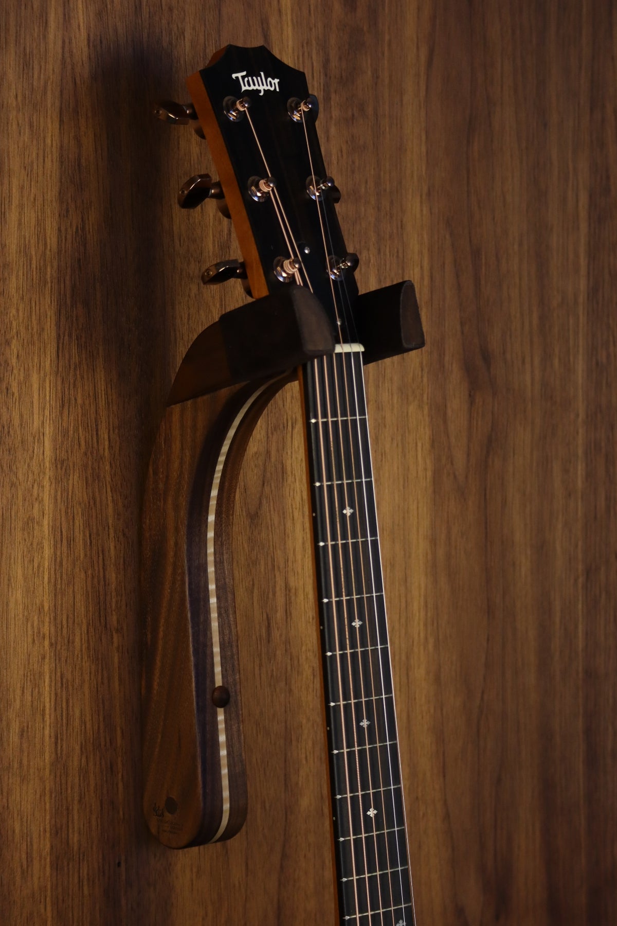 Walnut and curly maple wood guitar wall mount hanger installed on paneled wall with Taylor guitar